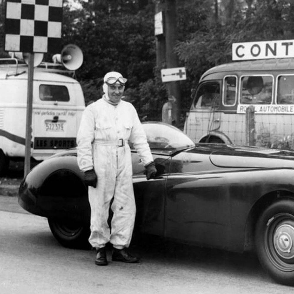 Man standing beside a vintage jaguar with two vehicles behind