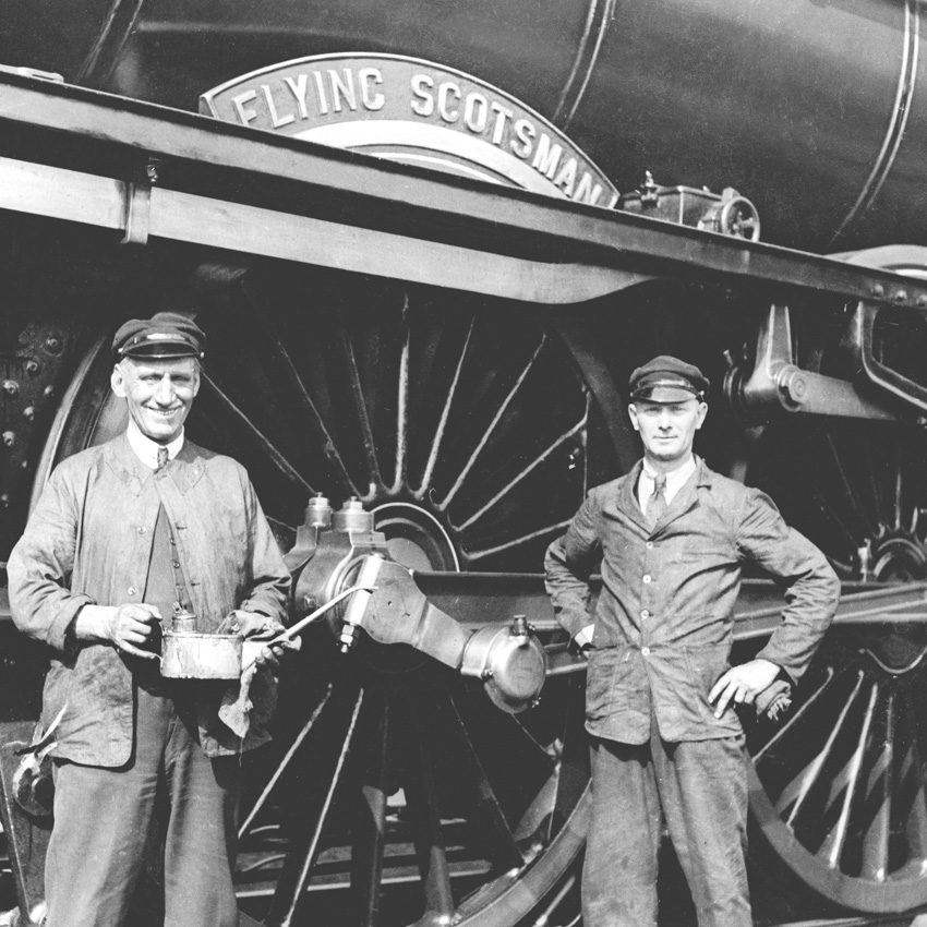 Two train workers standing beside flying scotsman wheel